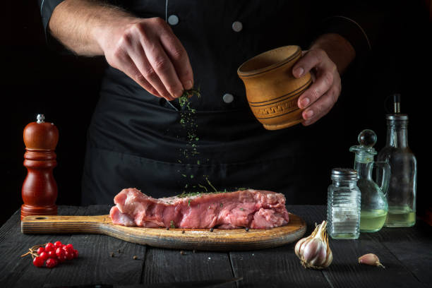 un chef professionnel prépare de la viande de veau crue. avant la cuisson, le chef ajoute un assaisonnement sec à base de plantes au bœuf. le plat national est préparé dans la cuisine du restaurant - veal calf meat baking photos et images de collection