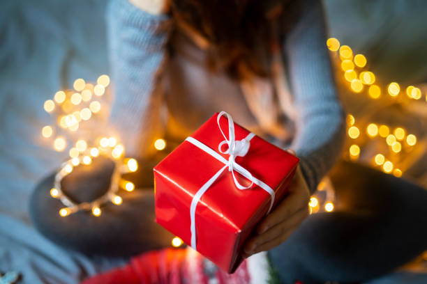 istock A person sitting on a bed holding up a small wrapped present in one hand 1429989032
