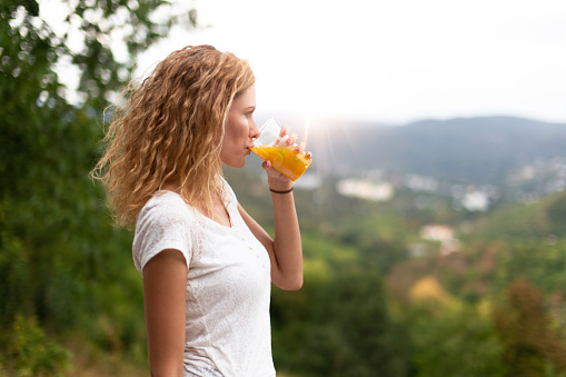 Young woman with curly hair drinking fresh juice at outdoors in nature, profile view