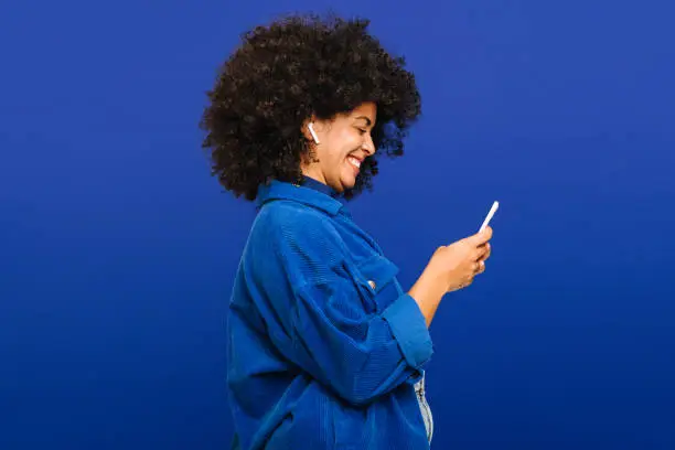 Photo of Carefree young woman playing music using a smartphone and earbuds