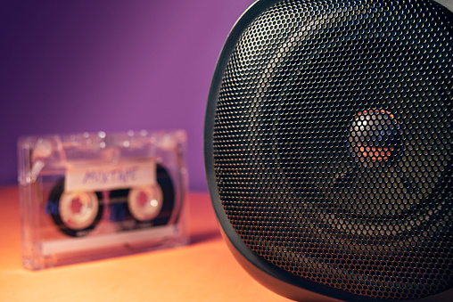 Close up stereo tape deck speaker in 90's color theme. A blank vintage audio cassette visible in the background.