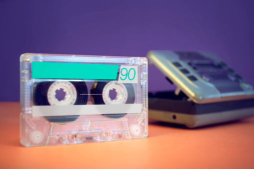 A retro audio cassette. A walkman visible in the background. 90's vintage electronics concept.