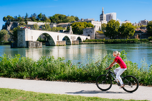 Woman cycling across from Pont Saint Benezet beside the River Rhone at Avignon in the Provence region of France.