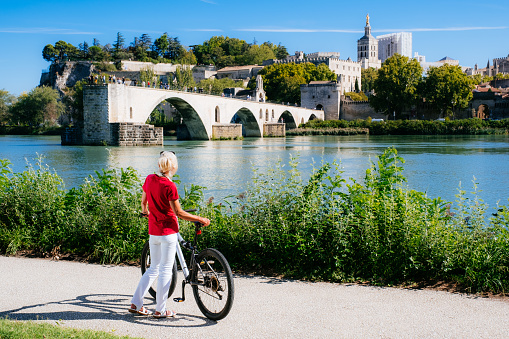 Woman cycling across from Pont Saint Benezet beside the River Rhone at Avignon in the Provence region of France.