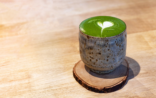 A cup of latte art matcha green tea in old style cup on wooden desk