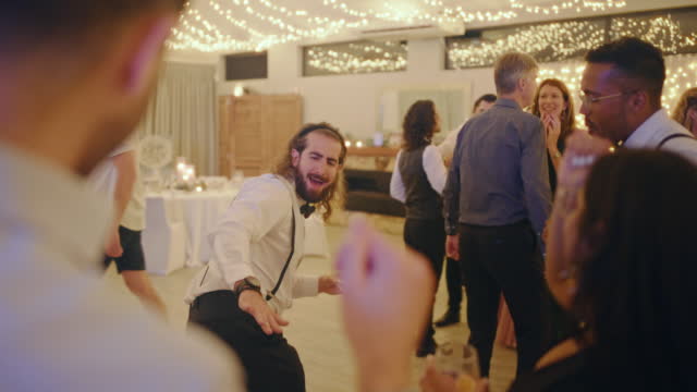 People dance and party at a wedding reception event with fun music and alcohol drinks. Crowd, friends or family goofy or comic dancing at a marriage celebration with happiness, energy and smiling
