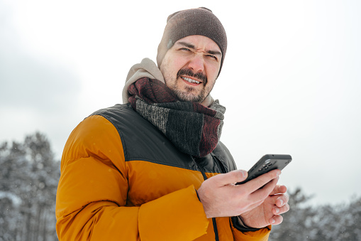 Young man in snowy winter forest using cell phone, close up
