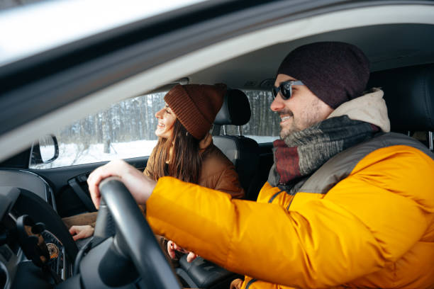 family couple sitting in car in winter clothes iin snow forest - winter driving imagens e fotografias de stock