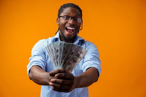 Portrait of amazed young man in casual shirt holding dollar banknotes against yellow background, close up