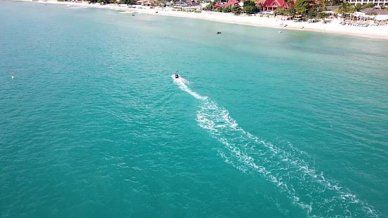 Aerial view of white sand beach and jet ski on the blue lagoon aqua sea. Aerial bird's eye view of jet ski cruising in high speed in turquoise clear water sea.
