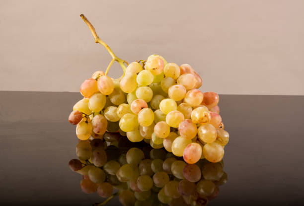 Juicy bunch of fresh grapes on black reflective background.
