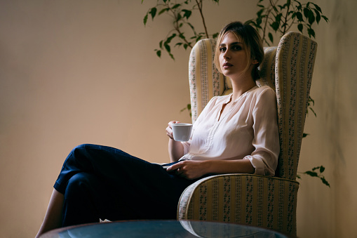 Caucasian woman sitting in armchair and drinking coffee