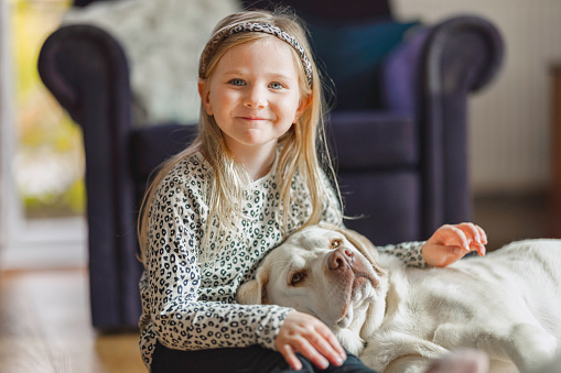 Natural light photo of a fair haired child cuddling up to her dog.