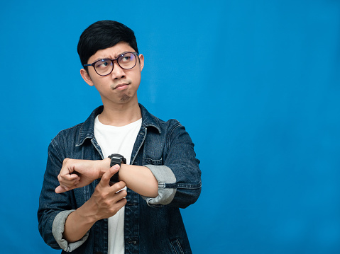 Young businessman hold his watch feels angry about late blue background