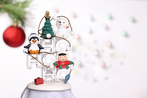 Happy snowman in warm clothes, red mittens, hat and scarf on rustic wooden table with shopping basket and Christmas tree at foreground. Christmas or winter background with defocused lights.