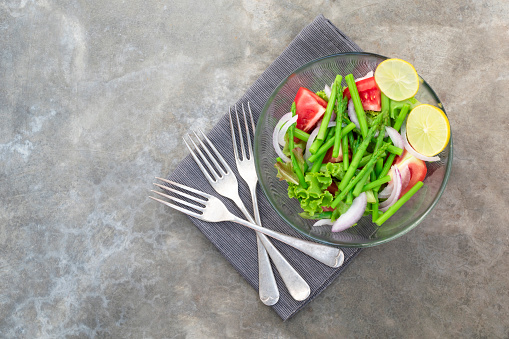 Asparagus salad has tomato onion lettuce in bowl on stone background, top view, healthy food concept.