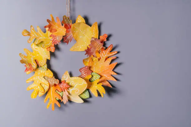 Homemade autumn yellow-red paper wreath on a gray wall background. Seasonal DIY