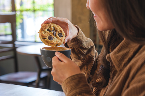 Closeup image of a young woman dipping a chocolate chip cookie into hot drinks