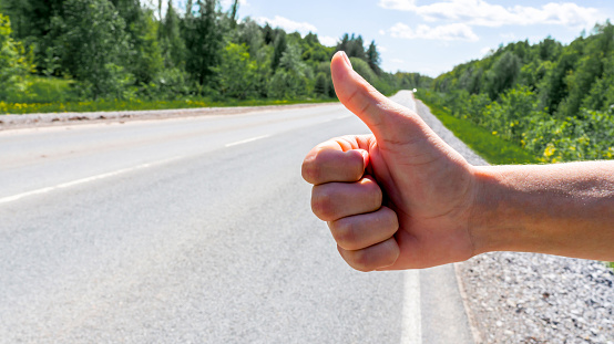 Hitchhikers give a thumbs up on the background of the road on a summer day in close-up. The concept of travel, tourism, hiking