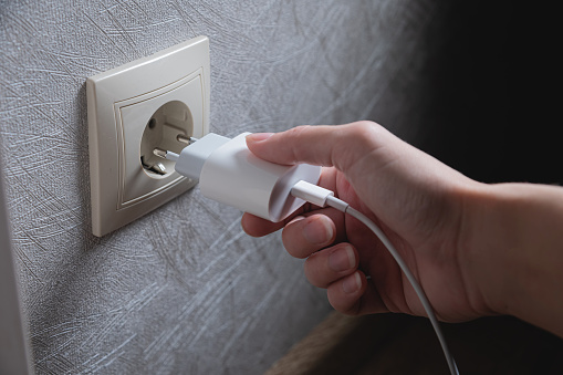 A young woman inserts a plug into a socket. A young woman plugs a charger or electrical appliance power cord into a socket. High quality photo.