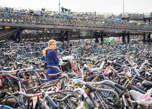 A woman wheeling her bike along, looking for a place to park it in a massive bike park near to Amsterdam's central train station in the city centre.