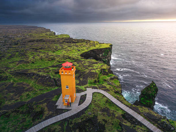 orange leuchtturm am rande der schwarzen felsklippe bei sonnenuntergang - snaefellsnes stock-fotos und bilder