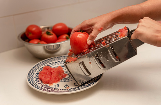 grating tomatoes through a metal grater in the kitchen
