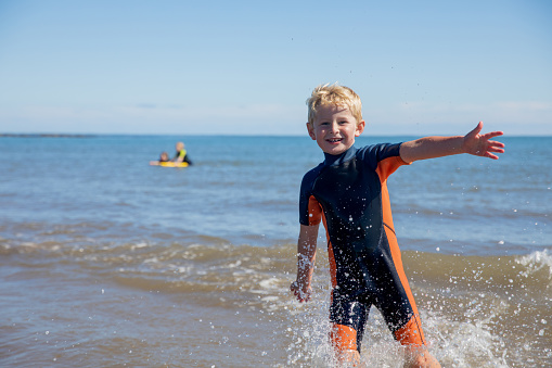 A young boy posing whilst standing in the sea smiling into the camera in Norhtumberland.