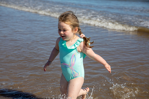 A young girl running out of the sea in Northumberland wearing a blue swim suit.
