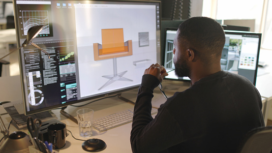 Stock photograph of a black male furniture designer working with CAD to design a contemporary chair, he’s working on a large computer screen.
