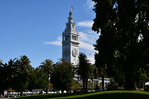 San Francisco, CA, USA - October 6, 2019: The clock tower of the San Francisco Ferry Building with an American flag flying at half mast.