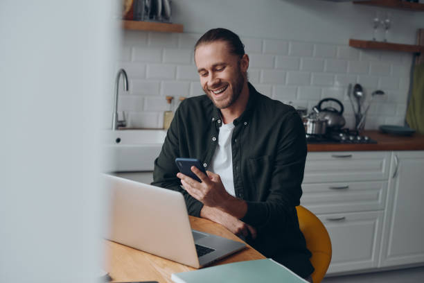 istock Cheerful young man using smart phone while working from domestic kitchen at home 1430033935