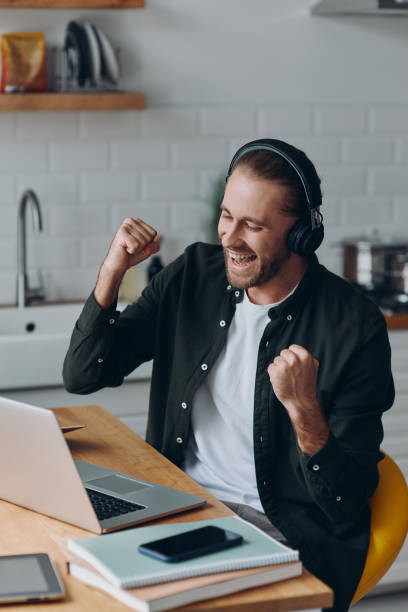 istock Excited young man in headphones gesturing while looking at laptop 1430034007