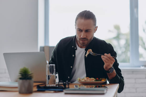 istock Busy young man using laptop and eating lunch while sitting at his working place in office 1430035754
