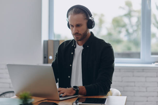 istock Confident man in headphones using laptop while sitting at his working place in office 1430035755