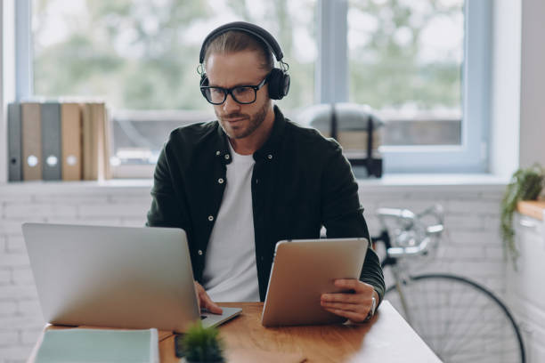 istock Concentrated man in headphones using technologies while sitting at his working place in office 1430038413