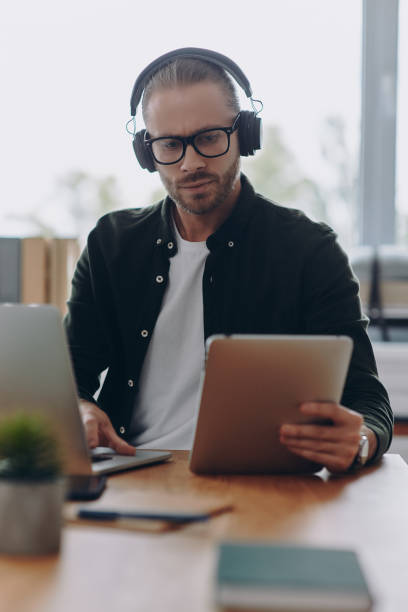 istock Confident man in headphones using technologies while sitting at his working place in office 1430039484