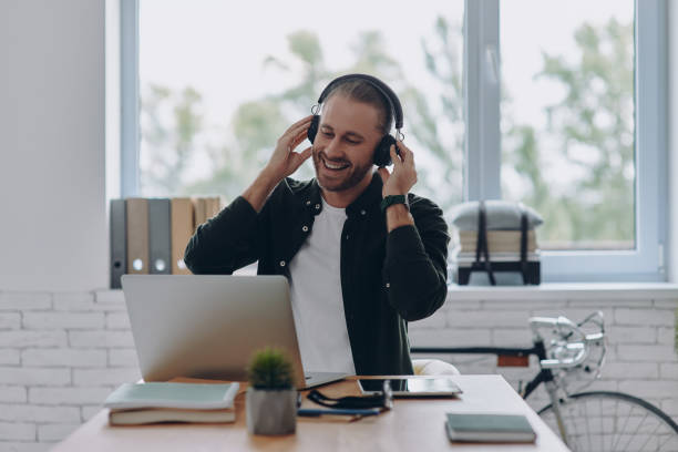 istock Happy young man in headphones using laptop while sitting at his working place in office 1430039486