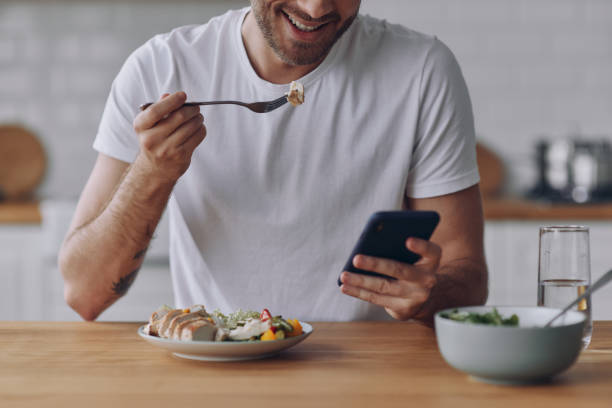 istock Close-up of man enjoying lunch and using smart phone while sitting at the kitchen 1430039489