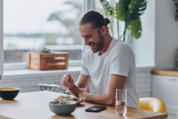istock Cheerful young man enjoying lunch while sitting at the kitchen counter at home 1430039610