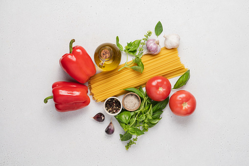 Spaghetti, tomatoes, red bell pepper, olive oil, garlic and basil on white background. Top view products for tomato paste preparation