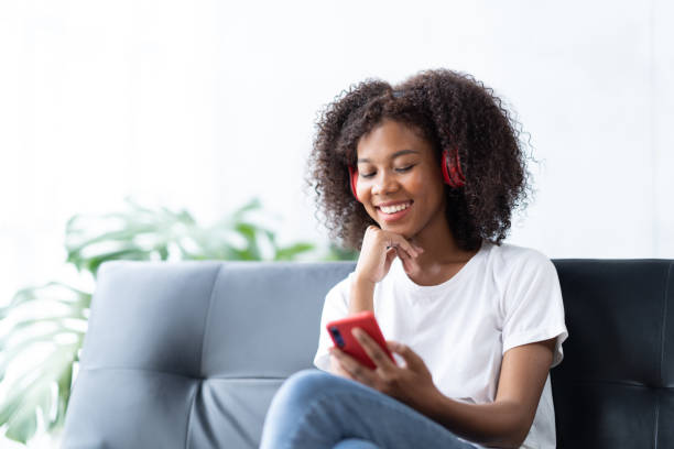 istock Smiling african american woman using smartphone at home, messaging or browsing social networks while relaxing on couch. 1430042793