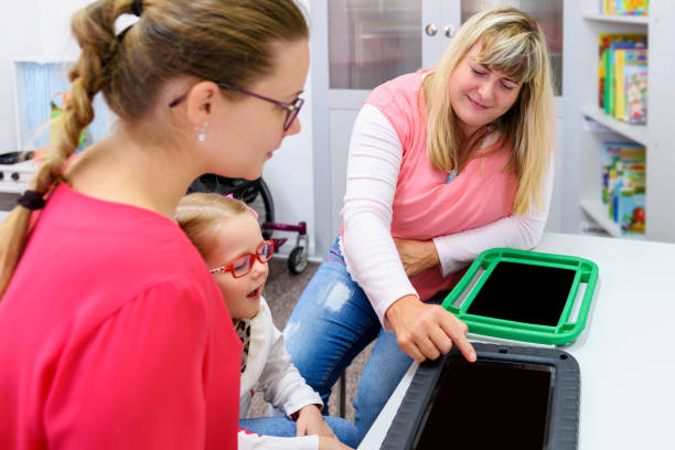 niña no verbal que vive con parálisis cerebral, aprendiendo a usar tabletas digitales para comunicarse. las personas que tienen dificultades para desarrollar el lenguaje o usar el habla usan dispositivos generadores de voz. - non verbal communication fotografías e imágenes de stock