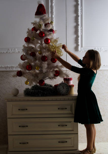 fique incrivelmente animado com o natal. garota criança perto da árvore de natal esperando o relógio da meia-noite. últimos preparativos. criança celebra o natal em casa. dia favorito do ano. celebração de natal - clock baby christmas small - fotografias e filmes do acervo