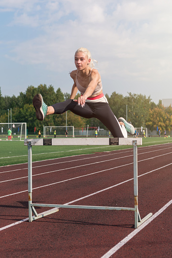 Young woman athlete runnner running hurdles at the stadium outdoors