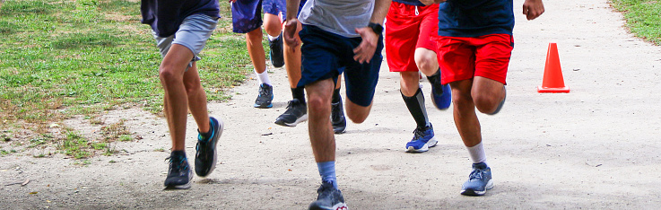A group of high school boys and girls cross country runners running and training together on a dirt path in a local park.