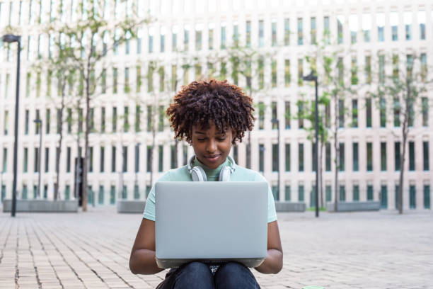 istock Young student sitting on the stairs outdoors and typing on her laptop 1430061951
