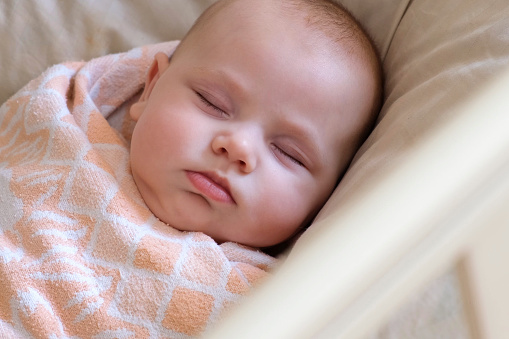 Safe Sleep Environment for Baby in Cotton Swaddle. Adorable Newborn Baby Sleeping Swaddled in Bed. Beauty New Born Taking a Nap in Crib. Swaddling For Infants. Little Kid Wrapped in Warm Blanket Relaxing. Close Up Portrait. Mother's Day Holiday.