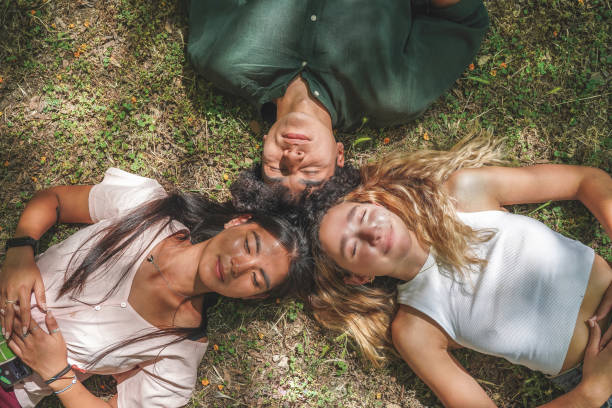 istock Group of three young multi-technic people lying down on ground in circle teenage students happy excited smile top angle view, outdoor 1430071126