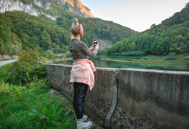Travel memories - concept. A woman with blond hair travels in a beautiful landscape and takes photos with her smartphone. Romania, Herculane. September, 29, 2022 irish travellers photos stock pictures, royalty-free photos & images